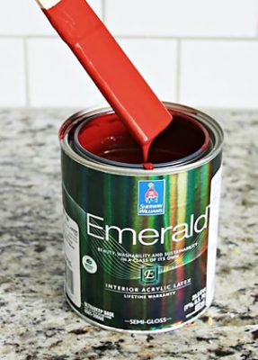 A stirrer dipped in a paint cannister S-W color featured: SW 6328 Fireweed.