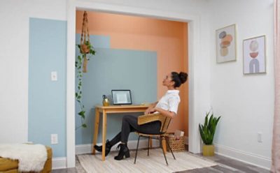 A woman sitting at a desk in front of an apricot, colorblocked wall. 