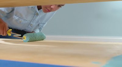 A woman painting a wooden surface with a mini roller. S-W color featured: SW 6486.