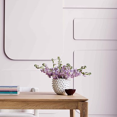 A workspace with textured walls painted Lite Lavender SW 6554 with a natural brown desk with book and flowers in a vase on top.