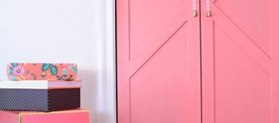 A set of wooden closet doors painted in pink with clear plastic and gold door handles.
