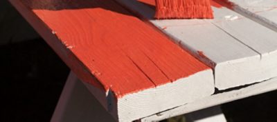 A wooden neutral tone picnic table being repainted in a bright red color.