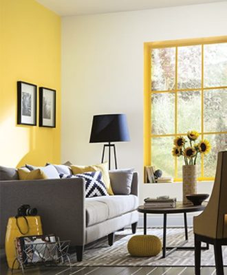 A bright yellow living room with gray couch that has lots of pillows and a round coffee table