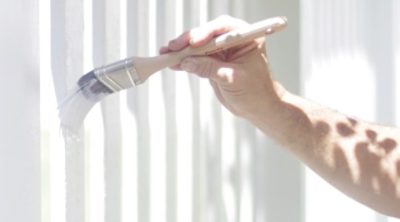 A man painting a white fence with fresh white paint. SW color featured: SW 7006 Extra White.