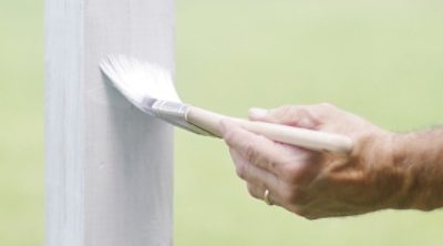 A man painting a white fence with fresh paint. SW color featured: SW 7006 Extra White.