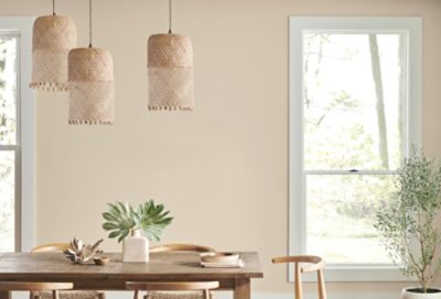 A beige dining room with woven chandeliers and farm table