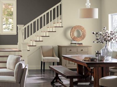 A stairway and dining room with neutral colors, farm table and bench