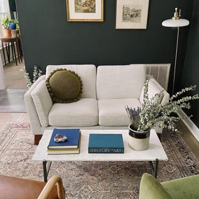 A dark green painted reading space with a cream sofa and picture frames. SW color featured: SW 7069 Iron Ore.