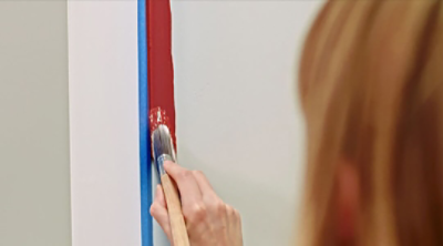 A woman painting the entryway wall red. S-W featured color: SW 7582 Salute