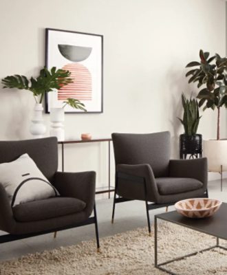 A neutral living room with light walls painted Silverpointe SW 7653 and dark gray chairs on a tan rug. There are many green plans in decorative pots and an abstract print on the wall.