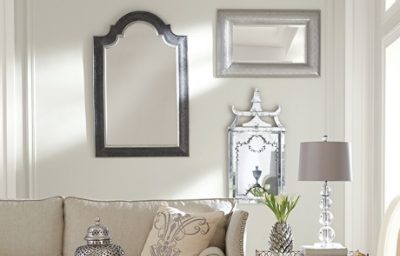 A beige living room wall with three mirrors and the top of a couch cushion