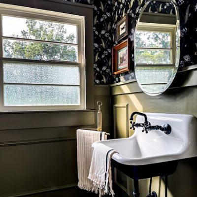 A vanity, large window, and dark blue wallpaper with flowers used in a bathroom