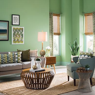 A light green living room that has a large area rug, decorative coffee table, and neutral-colored seating