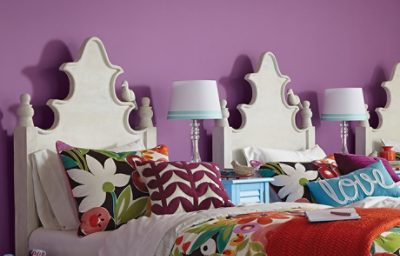 A cozy kid's bedroom with purple walls, floral sheets, and three twin beds