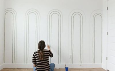 A woman painting arches on a bedroom wall. 