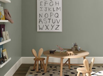 A nursery play area with round table, bookshelf and grayish-green wall