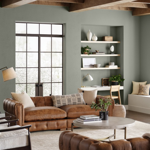 A living room with modern leather furniture and walls with recessed floating shelves painted Evergreen Fog SW 9130.