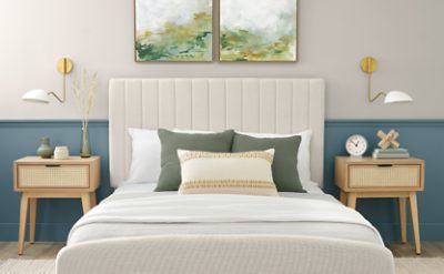 Bedroom with neutral and blue walls, neutral decor and nightstands, art above the bed with a couple throw pillows.