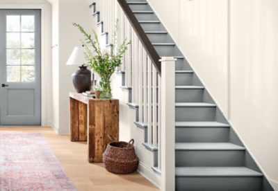 A white entryway with gray stairs and front door, and a wooden side table