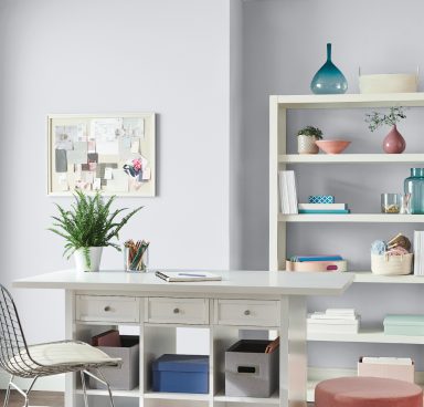 A light gray home office with white desk, chair, and bookshelf