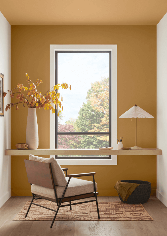 A floating writing desk in front of a window in a room with an accent wall and ceiling painted Bosc Pear SW 6390.