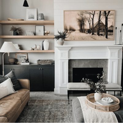 A fireplace with white painted shiplap next to inset natural wood open shelving. A dark wood cabinet sits below. Warm textures and furniture surround the fireplace. Credit: Instagram @ampir.decor.nn