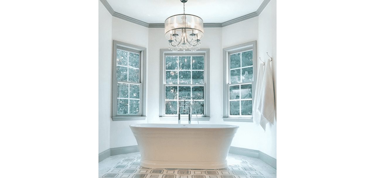 A large bright bathroom with 3 windows, chandelier and large white tub with walls painted in origami white sw 7636 by @design_build_sell_ga.