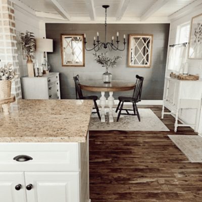 A kitchen dining area with a round table with 2 black chairs, chandelier and wall painted in peppercorn sw 7674 by @diapersanddecor.