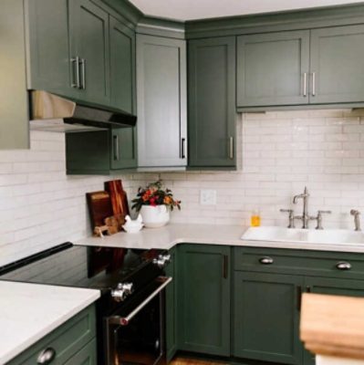 A kitchen with dark green shaker style cabinets and a white subway tile backsplash by @gardmercreativeco.