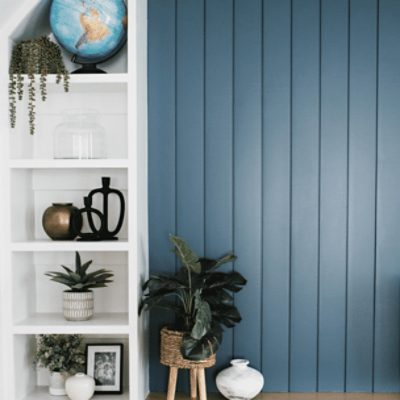 A white bookshelf next to a wood panel wall painted in needlepoint navy sw 0032 by @grace_into_joy.