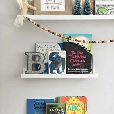 A wall painted in on the rocks sw 7671 by @lifeintheglens with white shelves with children's books on them.