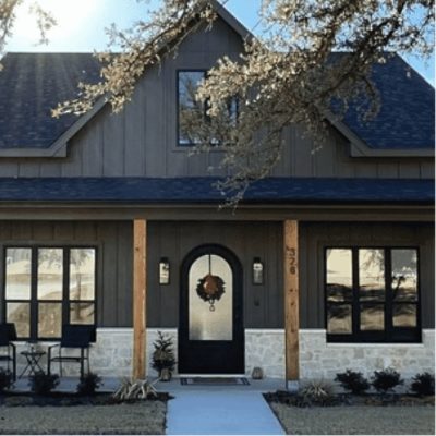 Dark green house with 3 windows on both sides of the front door and wooden pillars, by livinglarue.