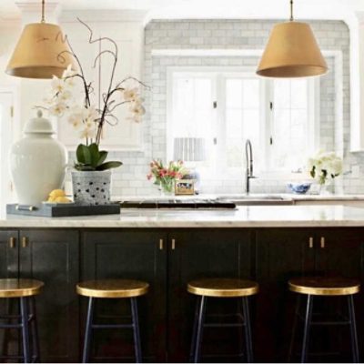 A kitchen with white brick walls & white cabinets with a large island painted black with brass accents by @mldesignskc.