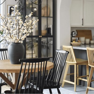 A kitchen with two wooden stools by a counter and a circular wooden table with black chairs and a vase with white flowers on top.