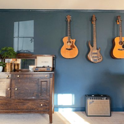 A multi-purpose room with a large wooden dresser and guitars mounted on a wall painted in mount etna sw 7625 by @sainhomes.