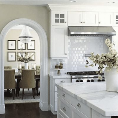 A kitchen with an island, white cabinets, arch and walls painted in natural linen sw 9109 by @studio7interiors.