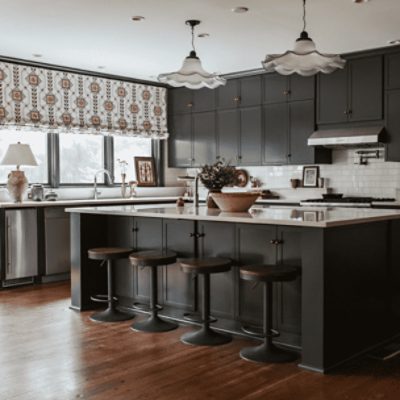 A large kitchen with an island and bar stools with cabinets painted in iron ore sw 7069 by @themisfithouse.