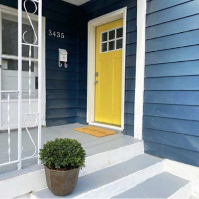 A front porch of a blue house with a front door painted a rich yellow by @thisflippinfamily.
