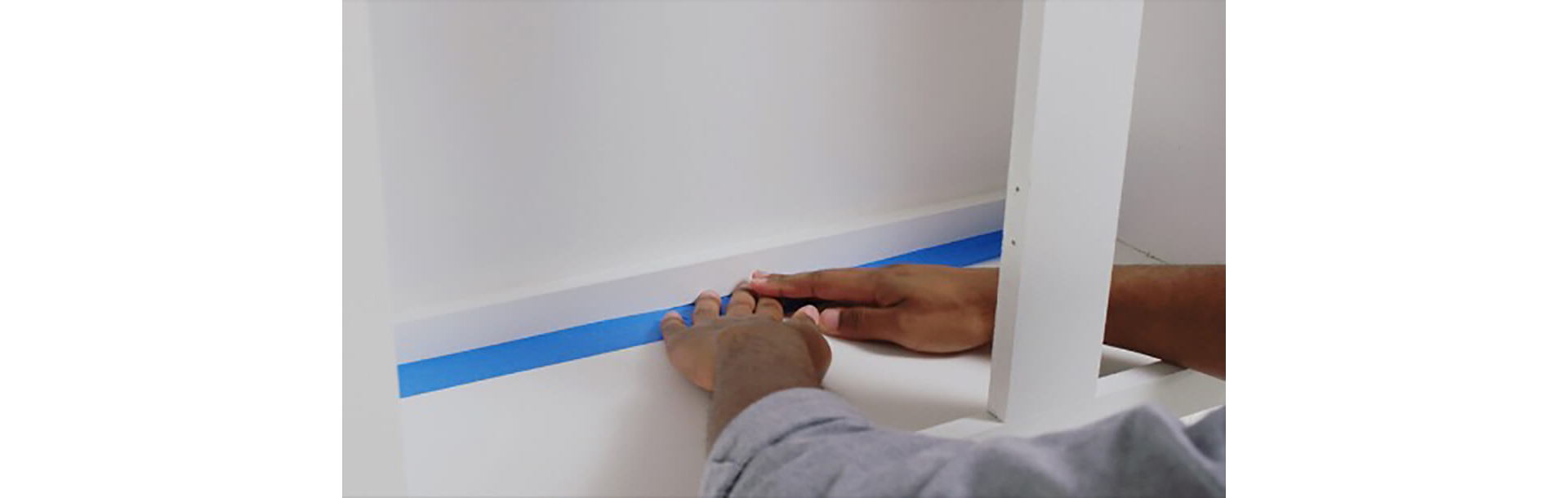 A man taping the inside of cabinets using painters tape 