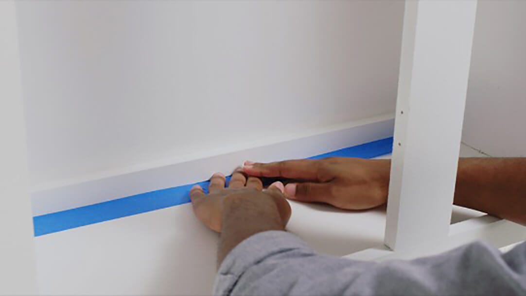 A man taping the inside of cabinets using painters tape 