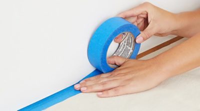 A person using blue masking tape from the floor to the ceiling of the room.
