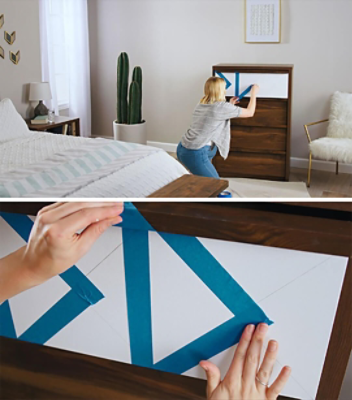 A woman is using blue painter's tape to prepare to paint a dresser