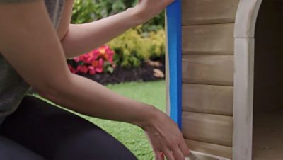 A woman placing tape on the side of a dog house for trim.