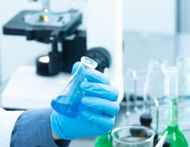 A person in a lab holding chemicals in a beaker.