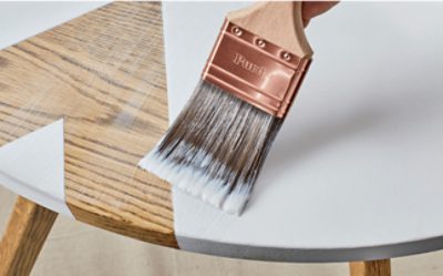 A person painting a wooden table with a Purdy paint brush.