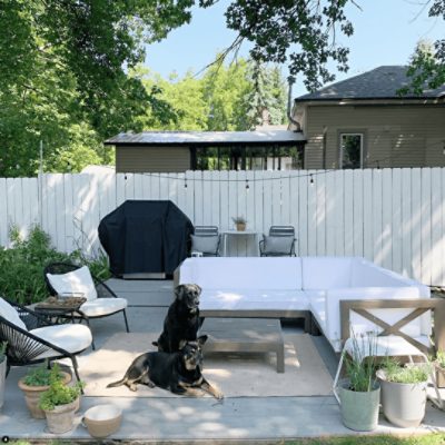An outdoor living area with a seating area, a grill next to a bistro table, on a patio in front of a wooden fence painted Alabaster white sw 7008.