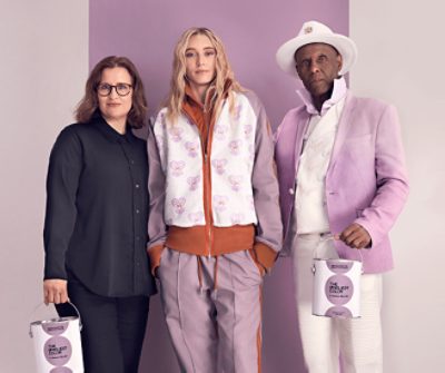 Sue Wadden, Paige Bueckers and Dapper Dan posing in front of a Radiant Lilac wall while holding The Loneliest Color branded paint cans.