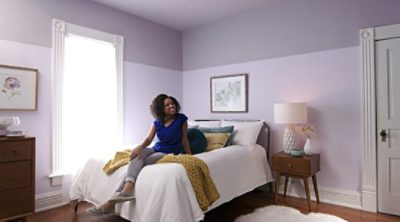 A woman sitting on a bed of a two toned painted bedroom. SW colors featured: SW 6827, SW 6268.