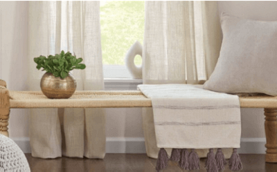A woven bench in front of a window with a pillow and tasseled blanket.