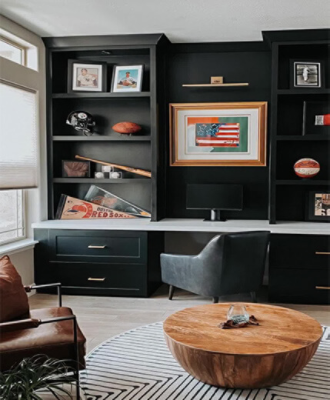 Office shelving painted in Tricorn Black with lots of sports decor, 2 chairs, large wooden coffee table, and printed rug.